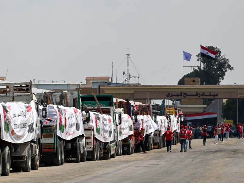 People walk past trucks loaded with aid for Gaza, waiting on the Egyptian side of the Rafah crossing on August 18, 2025.