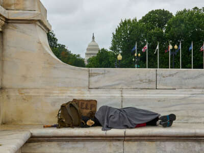 A homeless person sleeps on the bench with the U.S. Capitol building in the background.