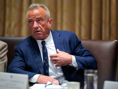 RFK Jk. is wearing a blue suit and is sitting in a chair.