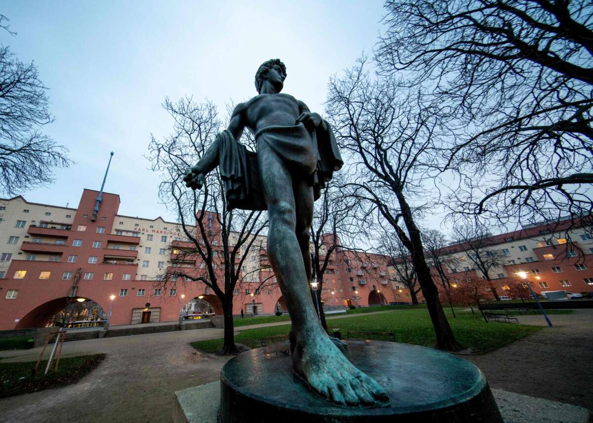 A statue is displayed in front of Karl-Marx-Hof, a red, several-story tall community owned apartment building in Vienna.