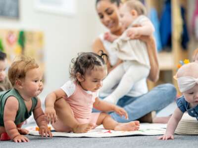 A group of babies is seen playing on the floor of their daycare classroom