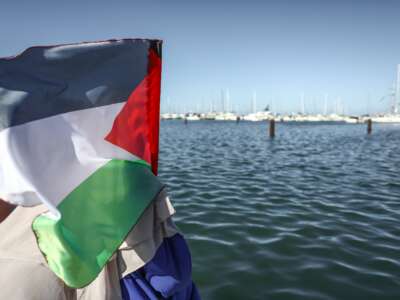 A Palestinian flag is waved as Tunisians gather outside the port of Bizerte in northern Tunisia on September 13, 2025, to support the Global Sumud Flotilla and show solidarity with the people of the Gaza Strip.