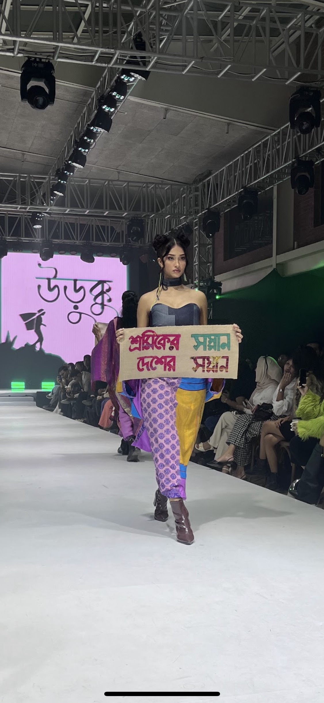 A model for upcycling fashion brand Urukku at Arka Fashion Week holds a sign that says, “The dignity of workers is the dignity of the nation.”