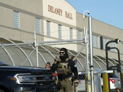 Immigration and Customs Enforcement (ICE) agents stand near a gate as they watch protestors at a demonstration in Newark, New Jersey May 7, 2025, outside Delaney Hall.