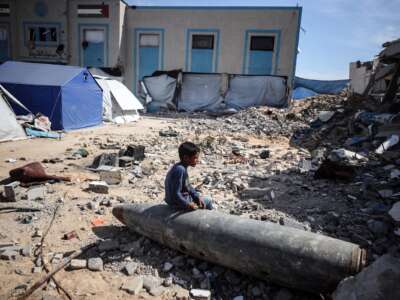 A displaced Palestinian boy sits on an unexploded shell inside a temporary camp for displaced Palestinians in central Gaza City, Palestine, on April 16, 2025/