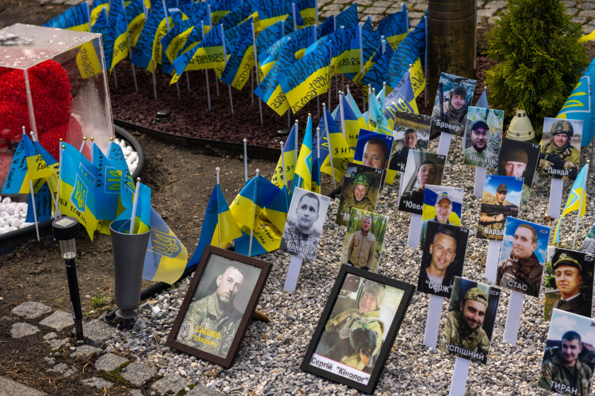 Ukrainian flags with text and portraits on sticks on the ground are pictured.