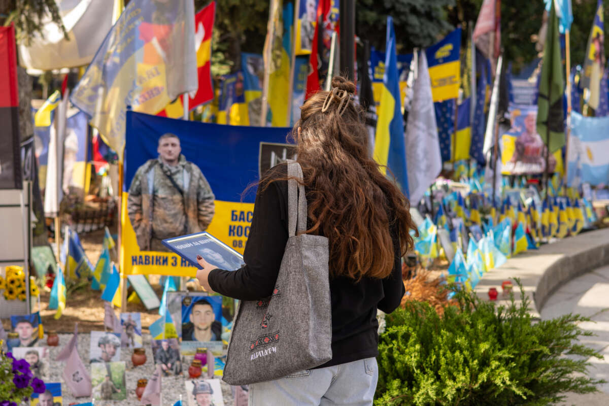 A woman holds a portrait in front of a memorial.