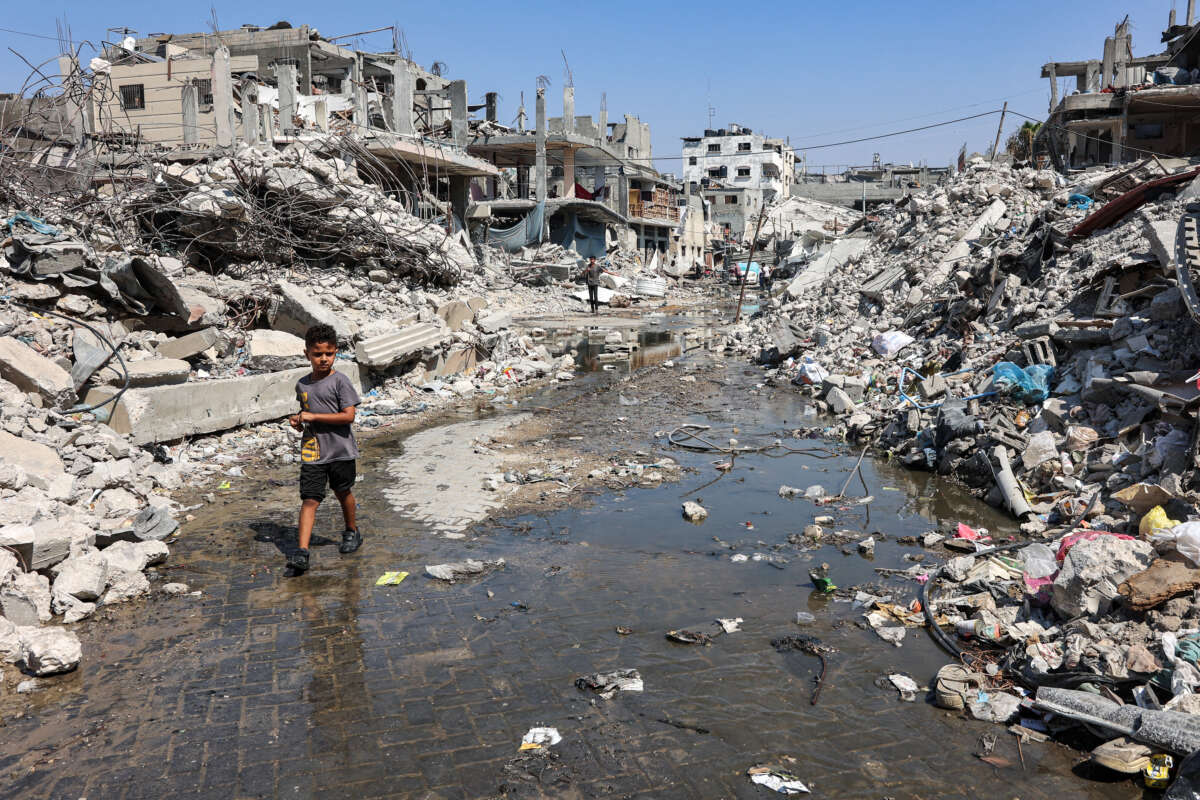 A boy walks through a puddle of sewage water past mounds of trash and rubble along a street in the Jabalia camp for Palestinian refugees in the northern Gaza Strip, on August 14, 2024.