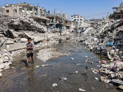 A boy walks through a puddle of sewage water past mounds of trash and rubble along a street in the Jabalia camp for Palestinian refugees in the northern Gaza Strip, on August 14, 2024.
