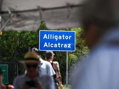 People around an Alligator Alcatraz sign are blurred out while the sign remains in focus.