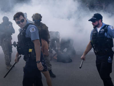 Chicago police officers and federal law enforcement agents stand in a cloud of tear gas deployed by federal agents against protesters in Broadview, Illinois, on October 4, 2025. The protest erupted after a Customs and Border Protection agent shot an anti-ICE protester in Brighton Park.