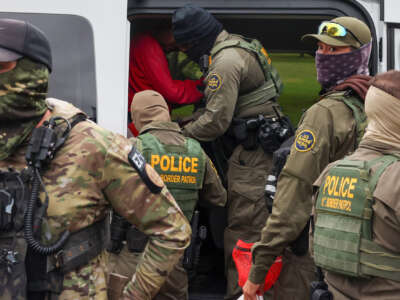 Federal agents detain a man and load him into a passenger van outside the Carpentersville Village Hall on October 15, 2025, in Carpentersville, Illinois.