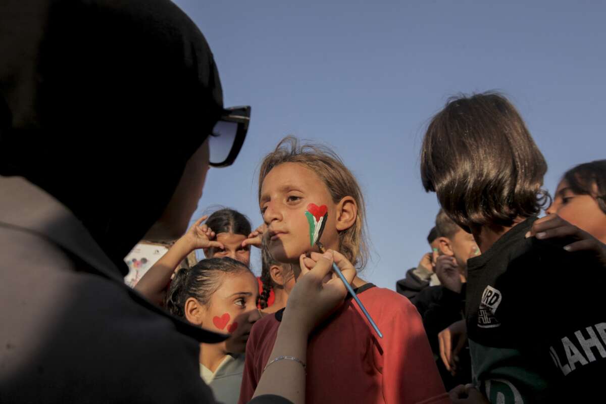 A volunteer paints a young girl's face as children gather among destroyed buildings in Al Shati refugee camp in Gaza City Gaza on November 23 2025.