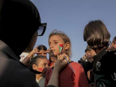 A volunteer paints a young girl's face as children gather among destroyed buildings in Al Shati refugee camp in Gaza City Gaza on November 23 2025.