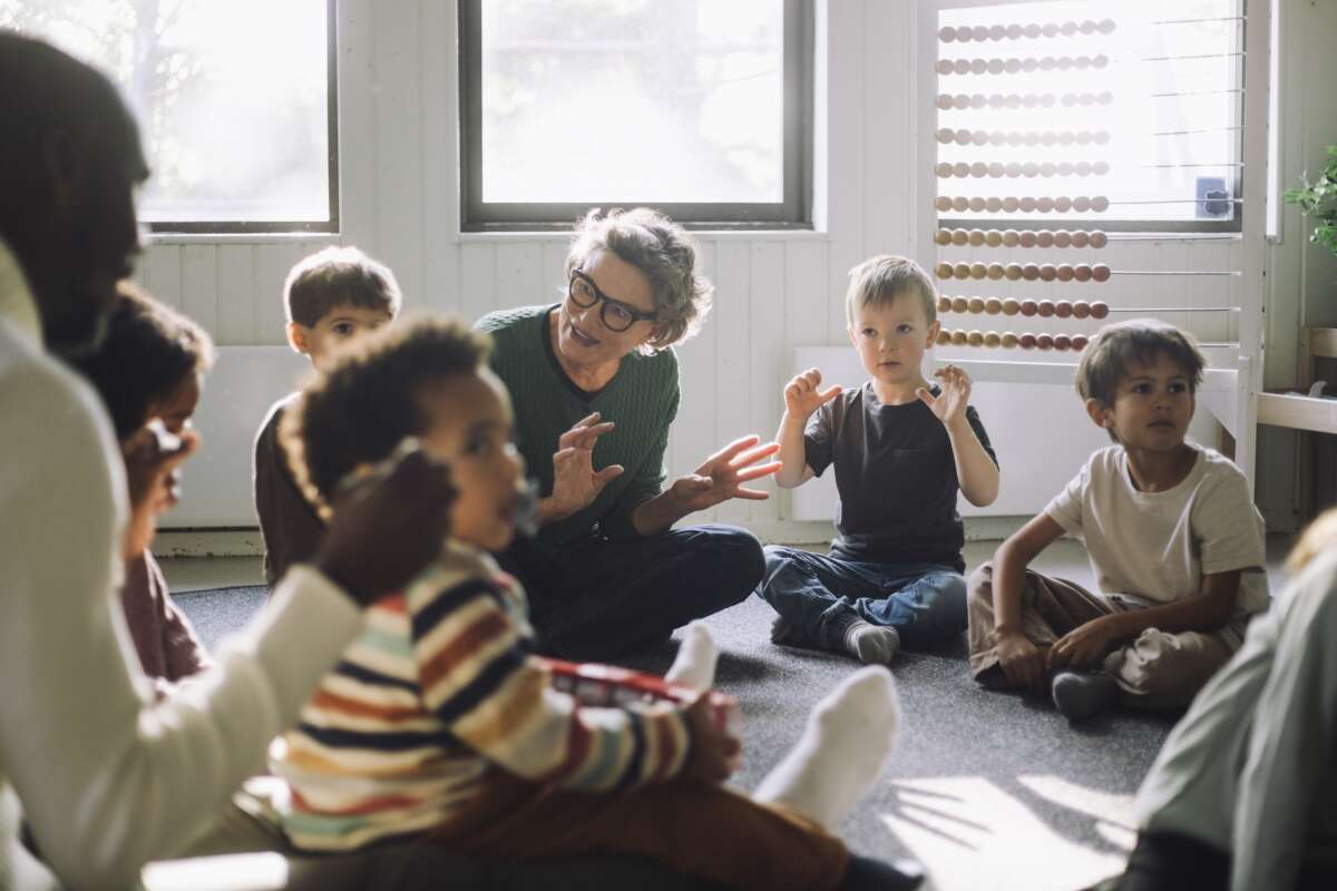 A teacher plays with a group of children while sitting in classroom