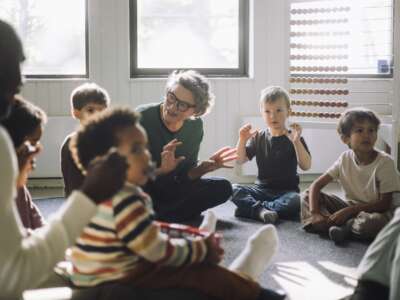 A teacher plays with a group of children while sitting in classroom
