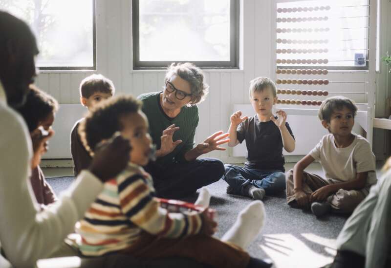 A teacher plays with a group of children while sitting in classroom