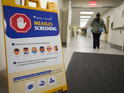A sign sits on the left corner of the image for measles screening while to the right is a woman in the background walking through a door