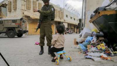 An armed Israeli soldier speaks with a child as other soldiers stand guard in the Old City of Hebron, in the occupied West Bank, on December 6, 2025. The area is routinely secured by troops to allow Israeli settlers to tour the city.