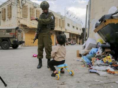 An armed Israeli soldier speaks with a child as other soldiers stand guard in the Old City of Hebron, in the occupied West Bank, on December 6, 2025. The area is routinely secured by troops to allow Israeli settlers to tour the city.