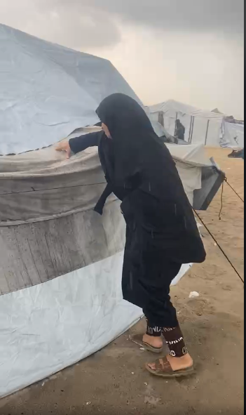 Ahlam Al-Raqab works to push away rainwater gathering on her tent, trying to prevent it from collapsing, on December 15, 2025.