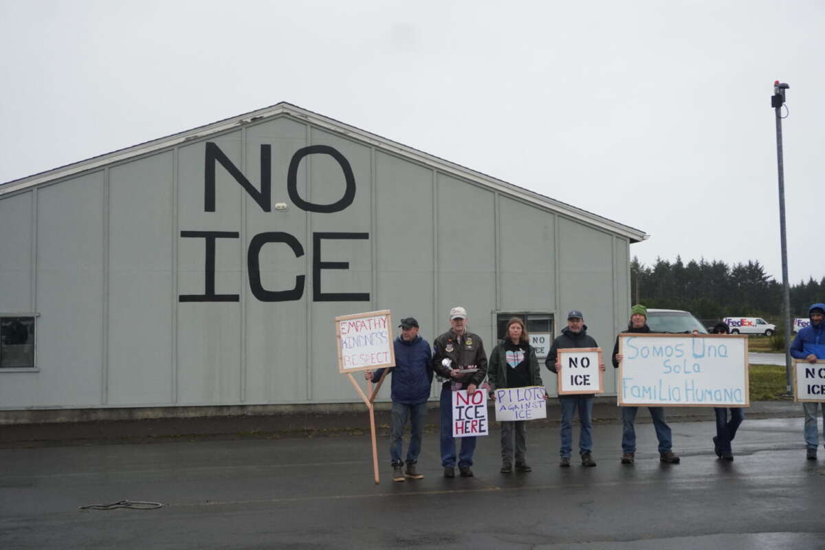 A group of local pilots and organizers stand by a hangar they have painted with “NO ICE”. “We are one human family,” a sign in Spanish held by one demonstrator reads.