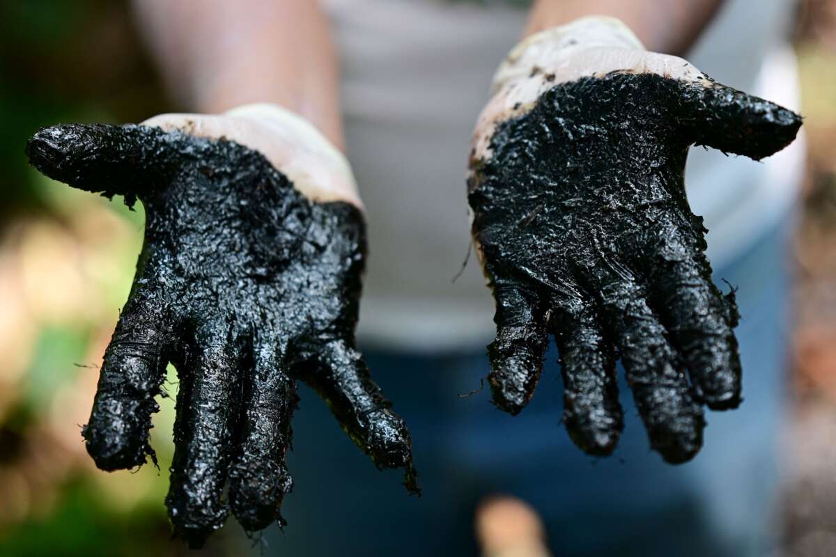 Ecuadorian activist Donald Moncayo Jimenez, chief coordinator of the Union of People Affected by Chevron-Texaco, shows his hands with hydrocarbon waste over an outdoor pool that was used in the process of drilling of the Aguarico 4 oil well, during a tour of the areas affected by the Chevron/Texaco oil company, in Lago Agrio, in the Sucumbíos Province, Ecuador, on January 14, 2023.