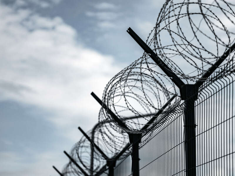 Barbed Wire Fence. Prison or border fence with razor wire against dark sky.