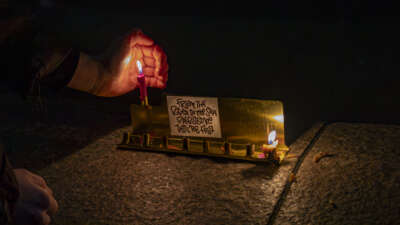 A person lights candles on a menorah with signs that say "From the river to the sea Palestine will be free" as Jewish groups gather at Columbus Circle on the first night of Chanukah during an action dubbed "Chanukah for Ceasefire" on December 7, 2023, in New York City.