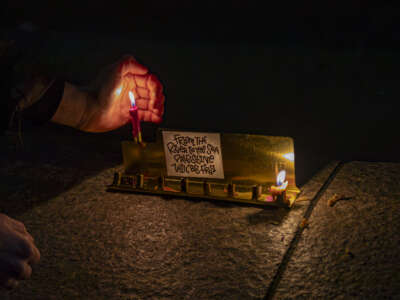 A person lights candles on a menorah with signs that say "From the river to the sea Palestine will be free" as Jewish groups gather at Columbus Circle on the first night of Chanukah during an action dubbed "Chanukah for Ceasefire" on December 7, 2023, in New York City.