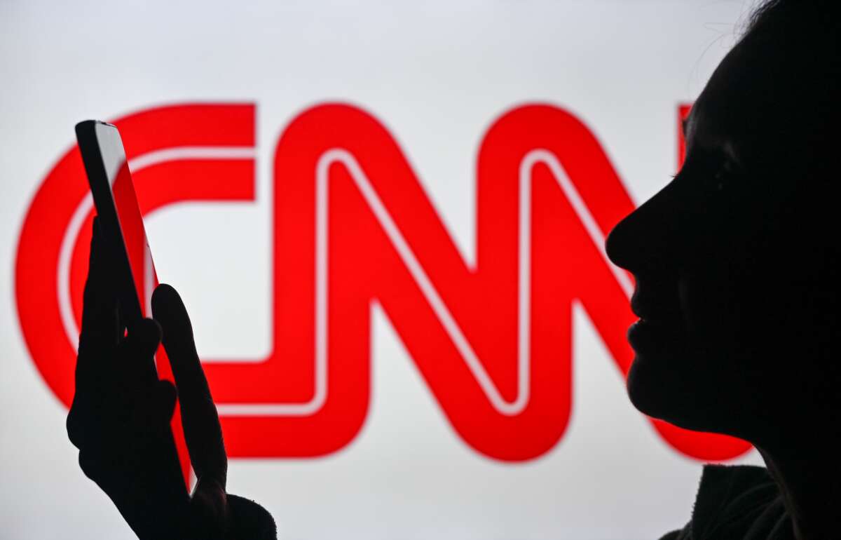 An image of a woman holding a cell phone in front of a CNN logo displayed on a computer screen, on April 29, 2024, in Edmonton, Canada. Soon, CNN will run live odds on world events where its viewers can gamble on them in real time on their smartphones.