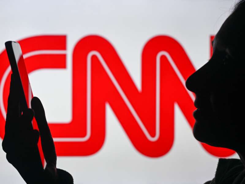 An image of a woman holding a cell phone in front of a CNN logo displayed on a computer screen, on April 29, 2024, in Edmonton, Canada. Soon, CNN will run live odds on world events where its viewers can gamble on them in real time on their smartphones.