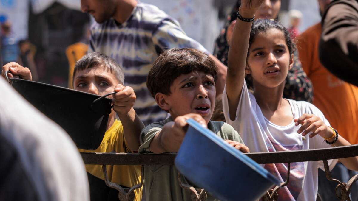 Children queue with pots to receive meals from a charity kitchen in Gaza City on July 14, 2025.