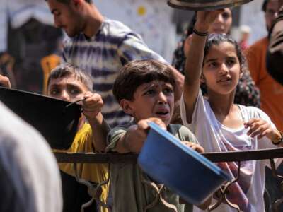 Children queue with pots to receive meals from a charity kitchen in Gaza City on July 14, 2025.