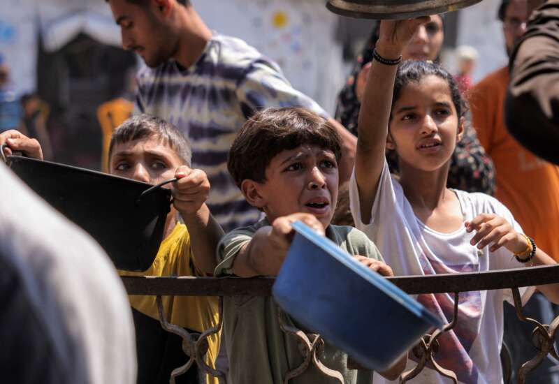 Children queue with pots to receive meals from a charity kitchen in Gaza City on July 14, 2025.