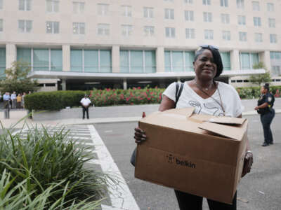 Recently laid off U.S. State Department employees carry boxes as they walk out of the Harry S. Truman Federal Building on July 11, 2025, in Washington, D.C.