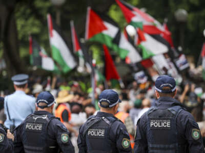 New South Wales police officers watch demonstrators hold flags and placards as they march during a Palestinian solidarity rally in Sydney, Australia, on October 12, 2025.
