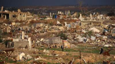 A man walks past homes and buildings destroyed by the Israeli military in the Nuseirat refugee camp in the central Gaza Strip, on December 13, 2025. Heavy rain has flooded tents and temporary shelters across Gaza, compounding the suffering of the territory's residents, nearly all of whom were displaced during more than two years of war.