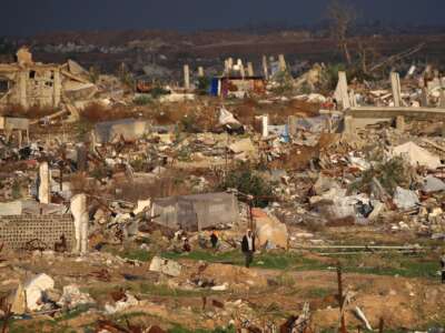 A man walks past homes and buildings destroyed by the Israeli military in the Nuseirat refugee camp in the central Gaza Strip, on December 13, 2025. Heavy rain has flooded tents and temporary shelters across Gaza, compounding the suffering of the territory's residents, nearly all of whom were displaced during more than two years of war.