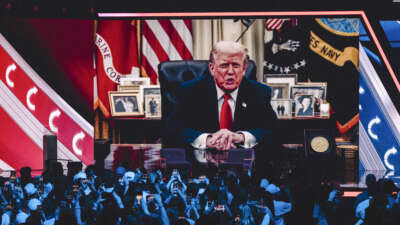 A prerecorded message from President Donald Trump is displayed on a screen after his son Donald Trump Jr. called him from the stage to address the audience by phone during Turning Point's annual AmericaFest conference in Phoenix, Arizona, on December 21, 2025.