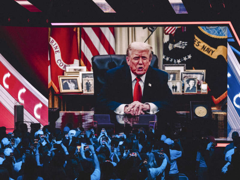 A prerecorded message from President Donald Trump is displayed on a screen after his son Donald Trump Jr. called him from the stage to address the audience by phone during Turning Point's annual AmericaFest conference in Phoenix, Arizona, on December 21, 2025.