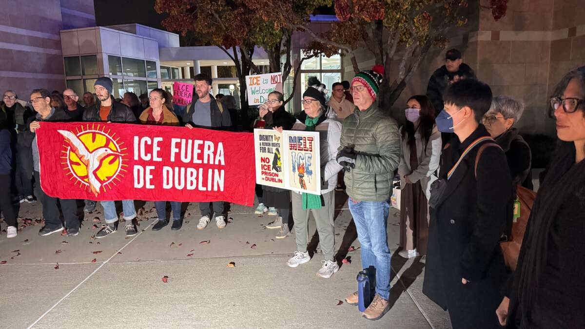 Dublin residents and immigrant justice advocates with the ICE Out of Dublin Coalition gather with signs and banners outside city hall in Dublin, California, before a city council meeting on December 16, 2025.