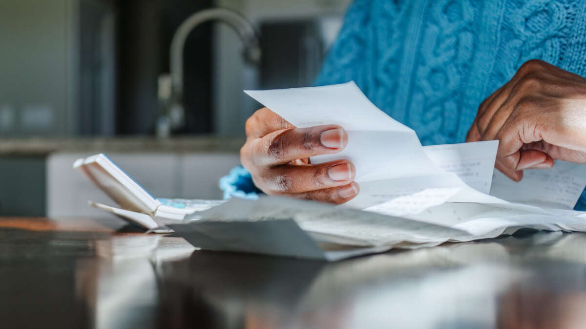 Close-up of black woman reviewing receipts at kitchen table with sunlight illuminating hands.