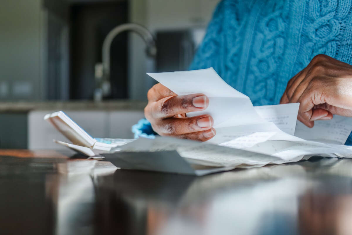Close-up of black woman reviewing receipts at kitchen table with sunlight illuminating hands.