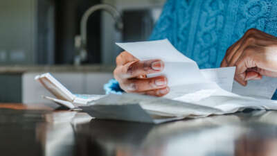 Close-up of black woman reviewing receipts at kitchen table with sunlight illuminating hands.