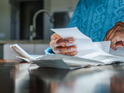 Close-up of black woman reviewing receipts at kitchen table with sunlight illuminating hands.