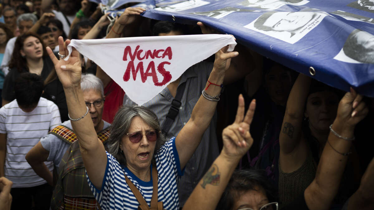 A woman holds a white handkerchief as people carry a banner with pictures of missing people, victims of Argentina's last dictatorship, during a demonstration to mark the 49th anniversary of the 1976 military coup, at Plaza de Mayo square in Buenos Aires, Argentina, on March 24, 2025.