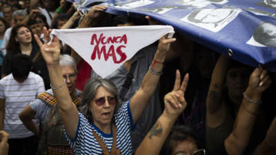 A woman holds a white handkerchief as people carry a banner with pictures of missing people, victims of Argentina's last dictatorship, during a demonstration to mark the 49th anniversary of the 1976 military coup, at Plaza de Mayo square in Buenos Aires, Argentina, on March 24, 2025.