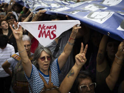 A woman holds a white handkerchief as people carry a banner with pictures of missing people, victims of Argentina's last dictatorship, during a demonstration to mark the 49th anniversary of the 1976 military coup, at Plaza de Mayo square in Buenos Aires, Argentina, on March 24, 2025.