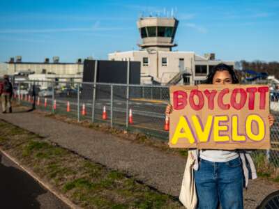 A protester holds a placard during a demonstration on April 17, 2025. Protesters marched in front of Tweed Airport, leaving placards hanging along the fence that condemned Avelo Airlines for its plans to assist the Department of Homeland Security in deporting migrants from Mesa, Arizona, out of the U.S.
